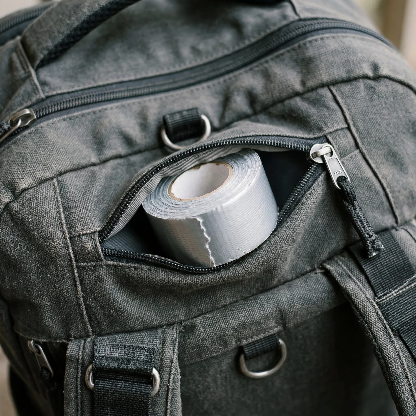 Small roll of silver duct tape tucked inside a travel bag zipper pocket, close-up, photorealistic, no text, no watermark, 16:9