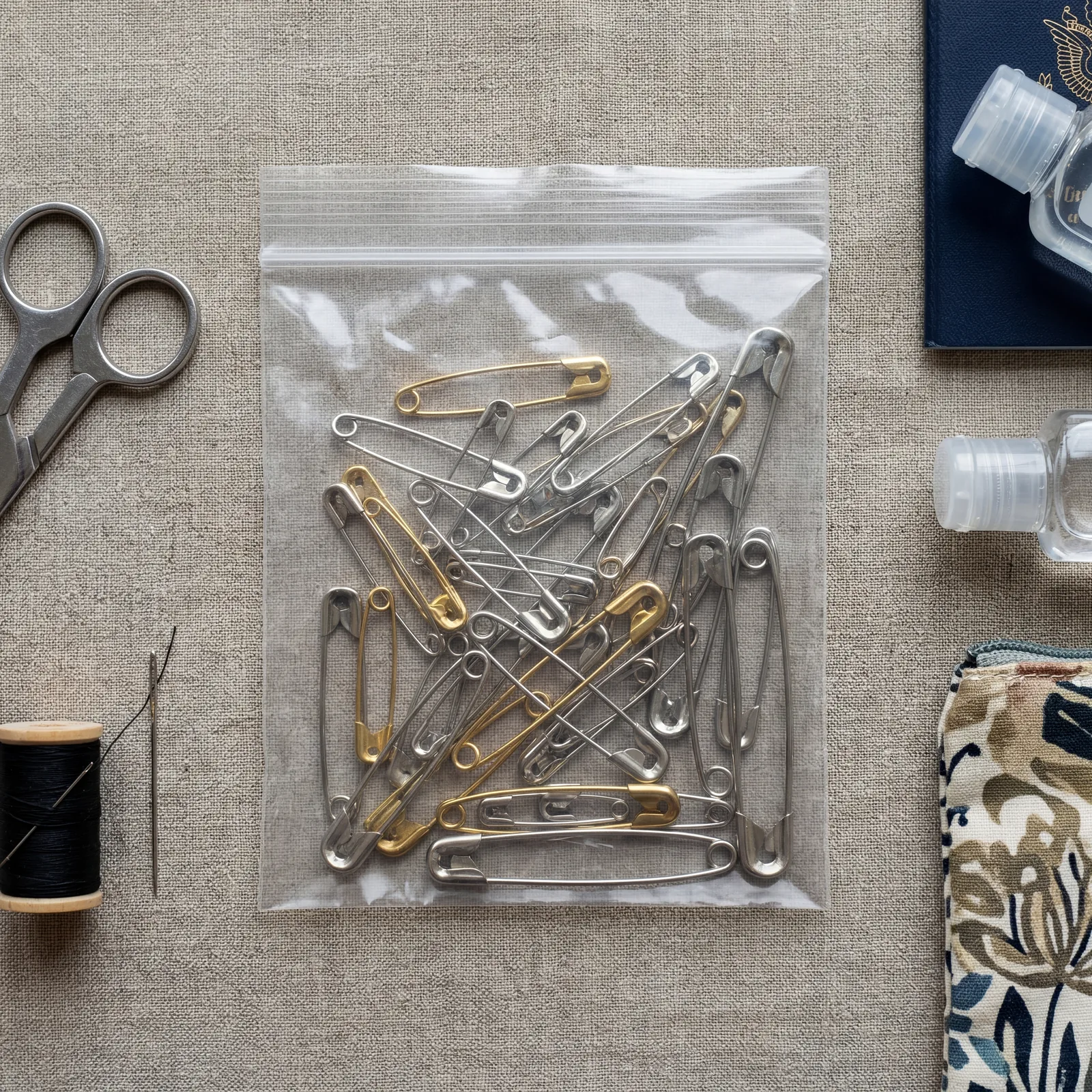 Small collection of safety pins of different sizes in a clear ziplock bag, travel accessories flat lay, photorealistic, no text, no watermark, 16:9