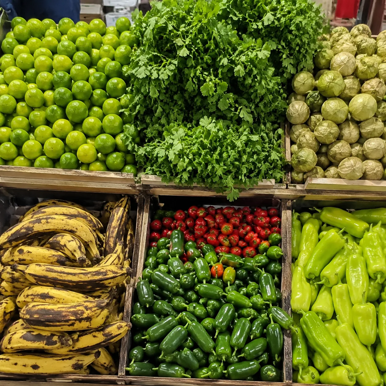 Realistic editorial photo of colorful produce crates with limes, cilantro, tomatillos, plantains, and peppers in a Latin