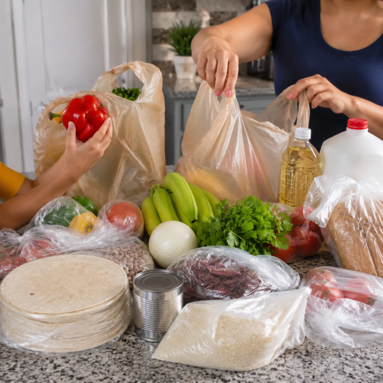 Realistic editorial photo of a home kitchen counter covered with grocery bags, tortillas, produce, pantry staples, and f