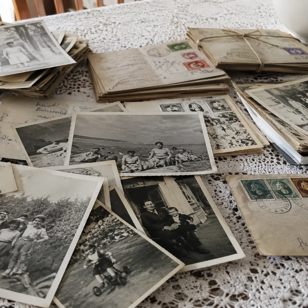 Realistic editorial photo of old family postcards, black and white photos, and stamped envelopes on a dining table, arch