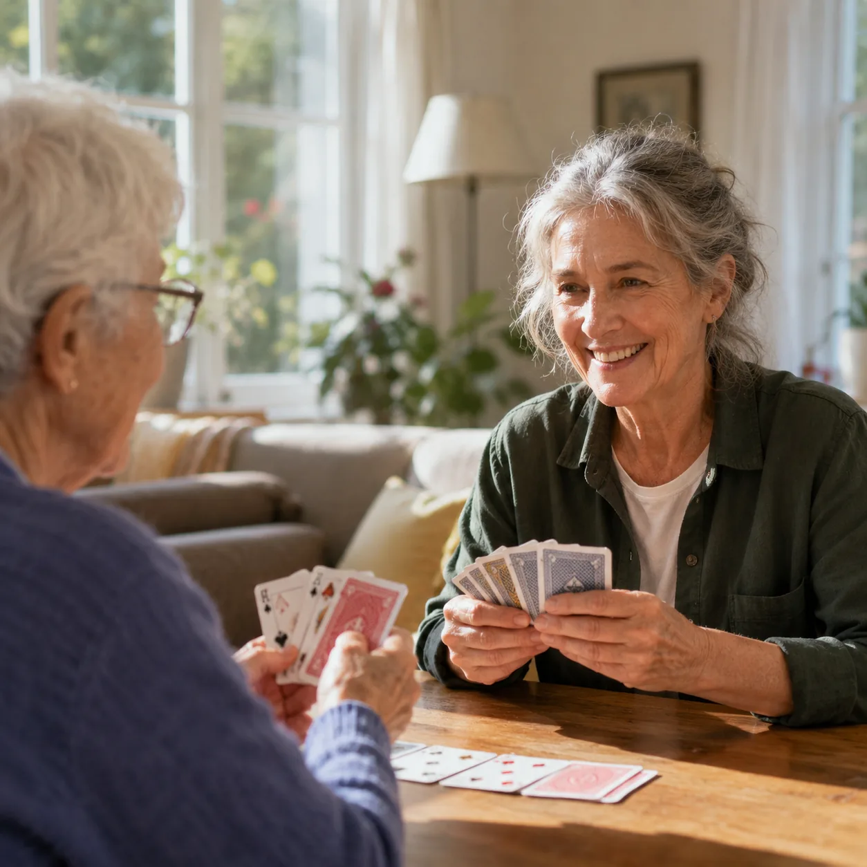 Realistic editorial photo of an older care companion playing cards with a senior client in a sunny living room, practica