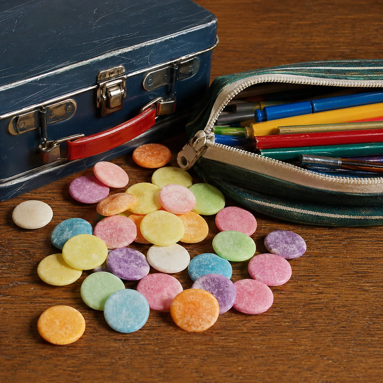 Realistic editorial photo of colorful round candy wafers scattered beside a lunchbox and pencil case, practical 1970s ch