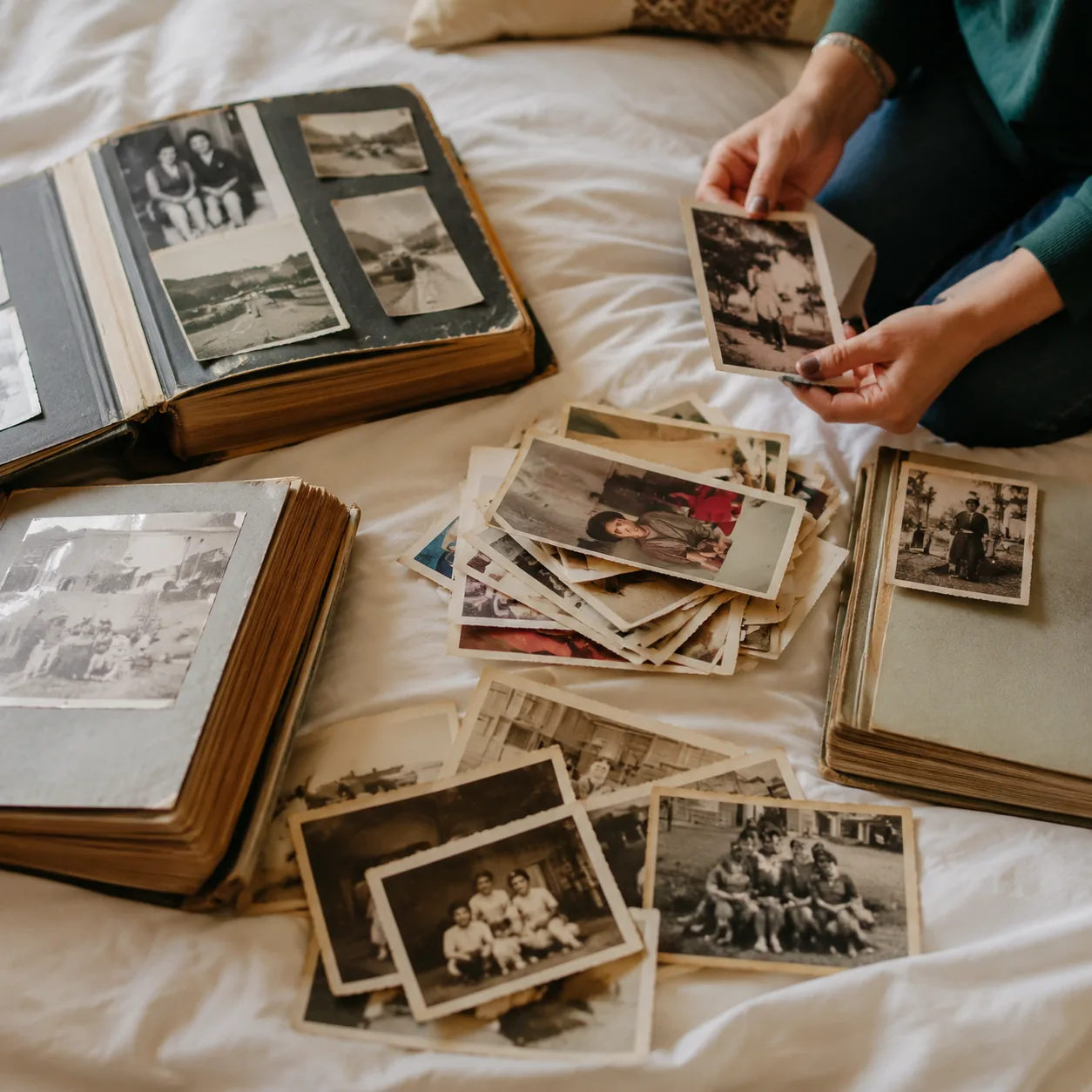 Realistic editorial photo of old photo albums and loose family pictures spread carefully on a bed, warm natural light, r