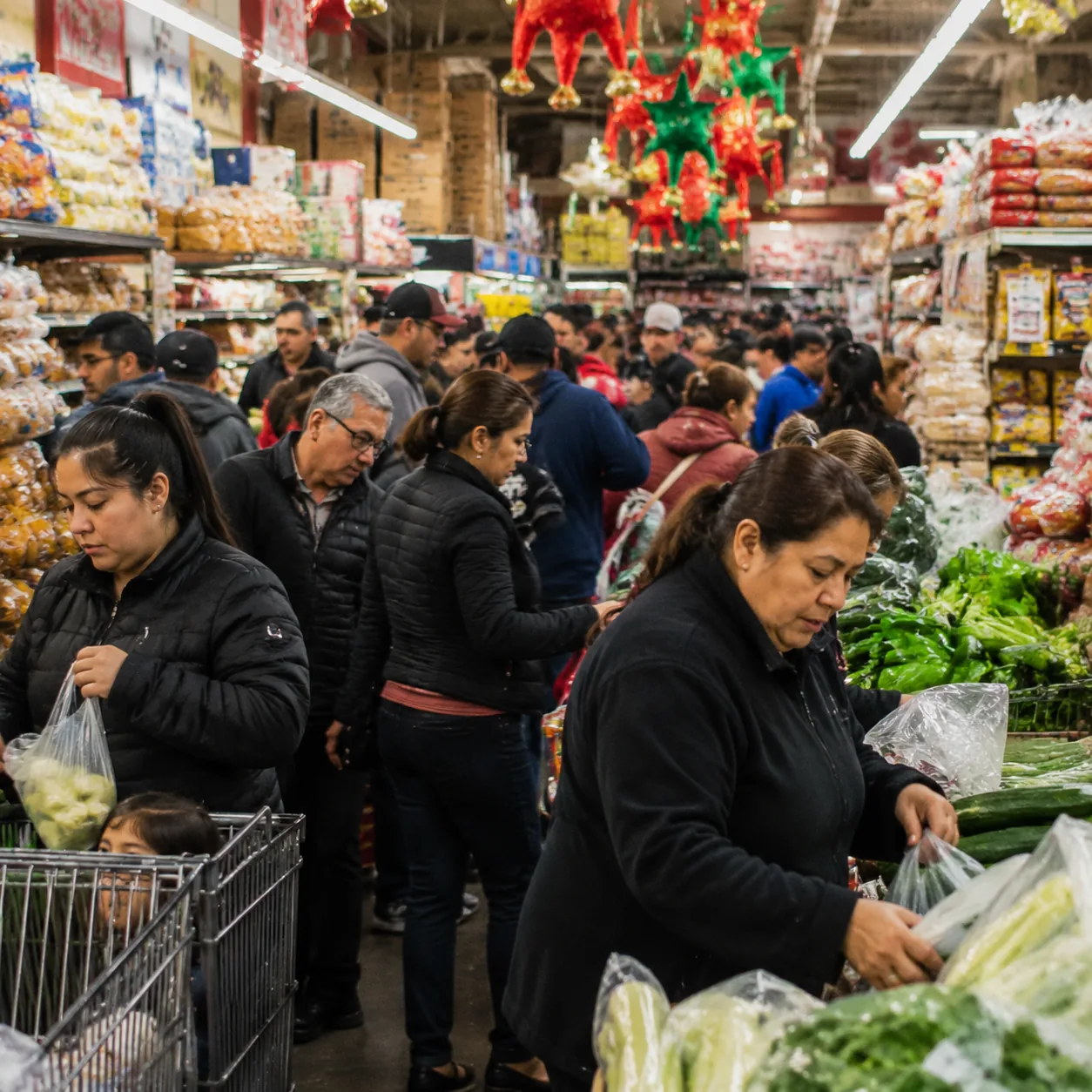 Realistic editorial photo of a crowded Latino grocery store aisle before a holiday with families shopping for produce an