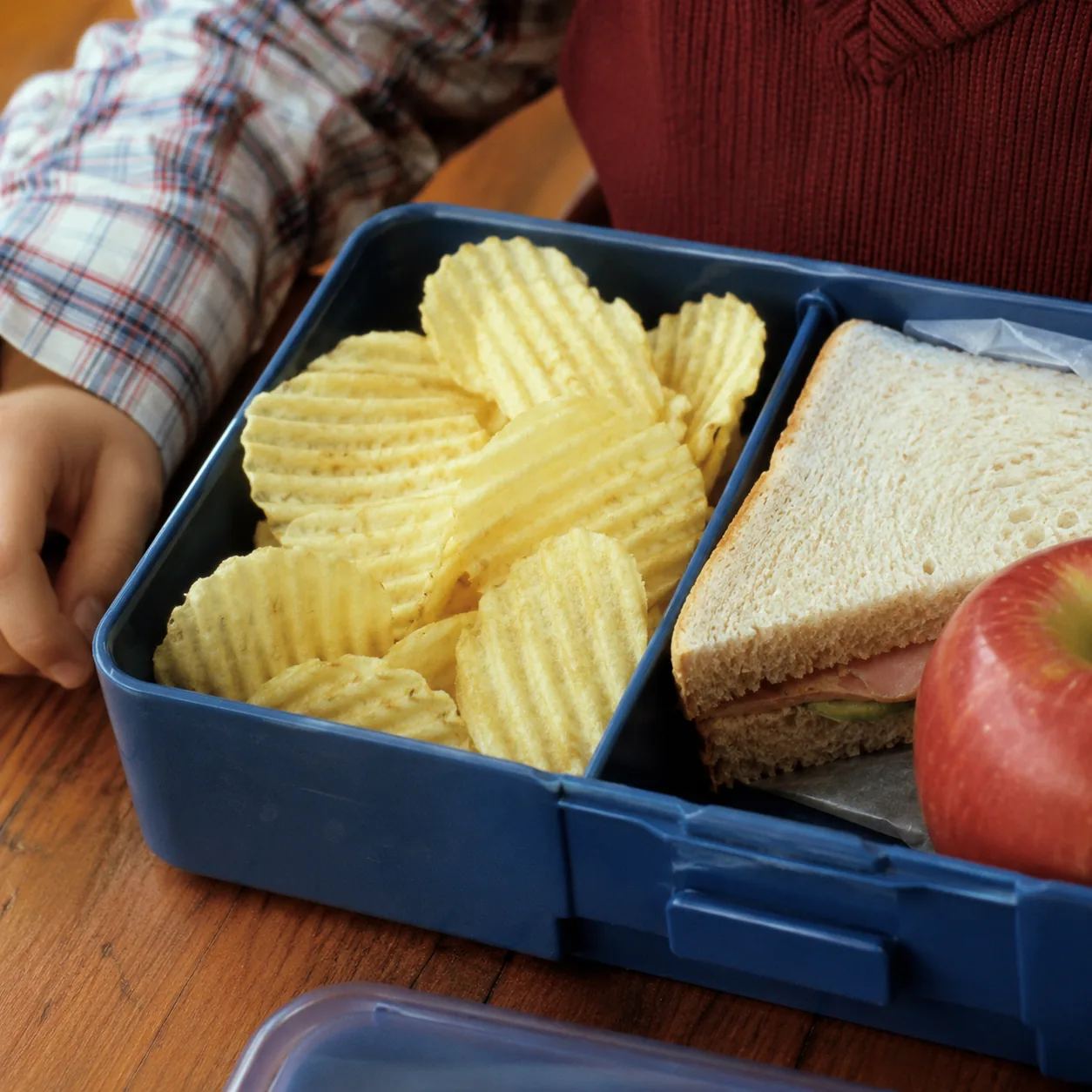 Realistic editorial photo of thick ridged potato crisps in a lunchbox compartment beside a sandwich, practical 1980s sch