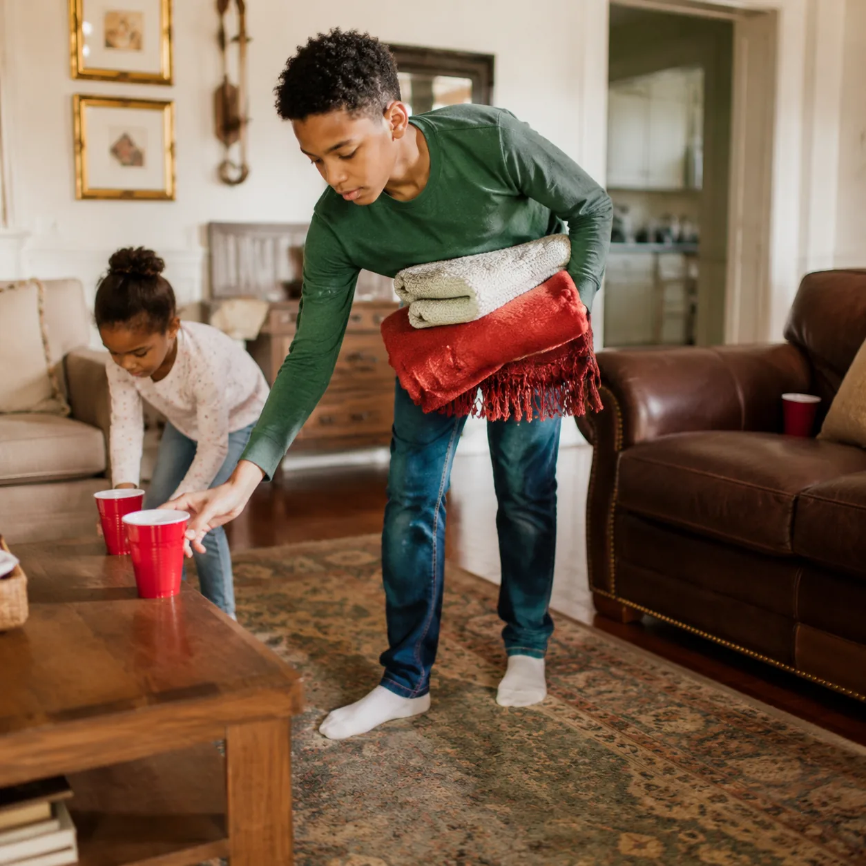 Realistic editorial photo of children picking up cups and folded blankets after a family gathering in a living room, war